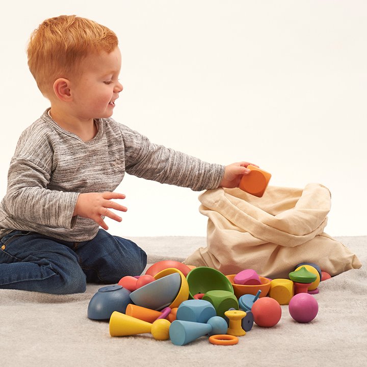 Child with bag of Tactile smooth solid beechwood loose parts in the seven colours of the rainbow