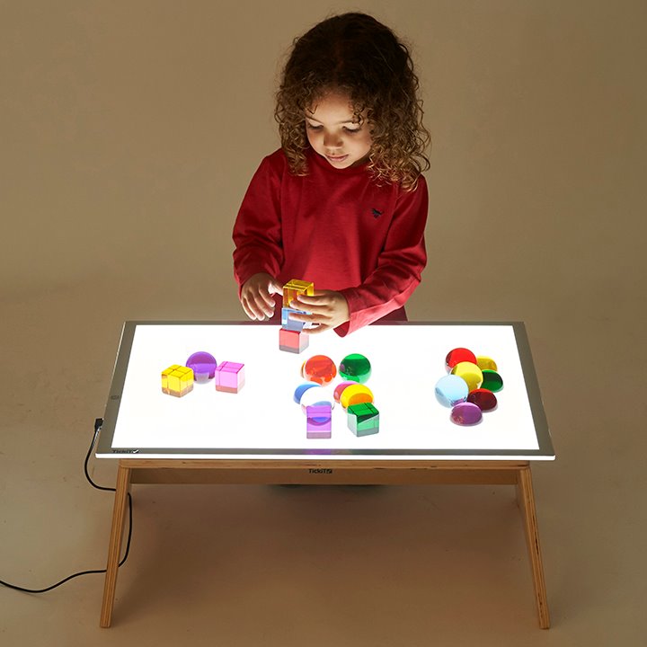 Little girl playing with shapes on light panel table