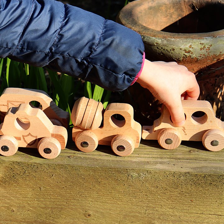 Little hand playing with a line of wooden vehicles in an outdoor environment