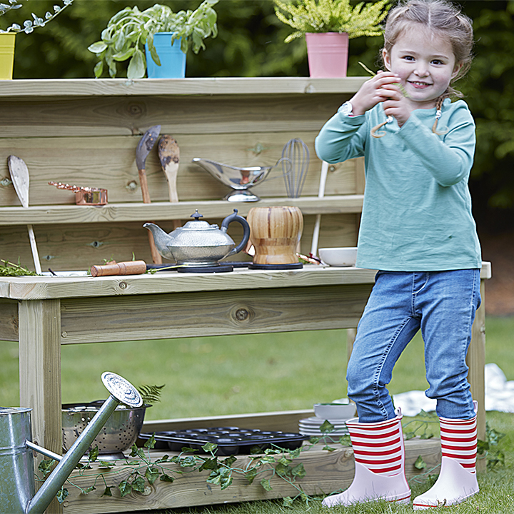 Little girl posing in front of mud kitchen with wellies on