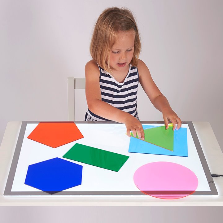 Little girl organising acrylic shapes on light panel